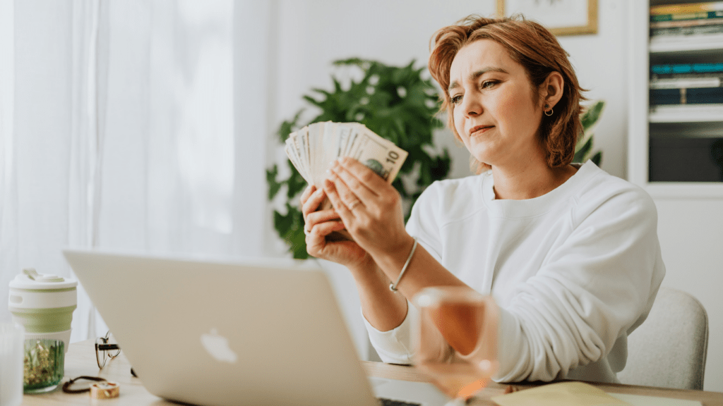 A person sitting in front of a laptop with money in their hand