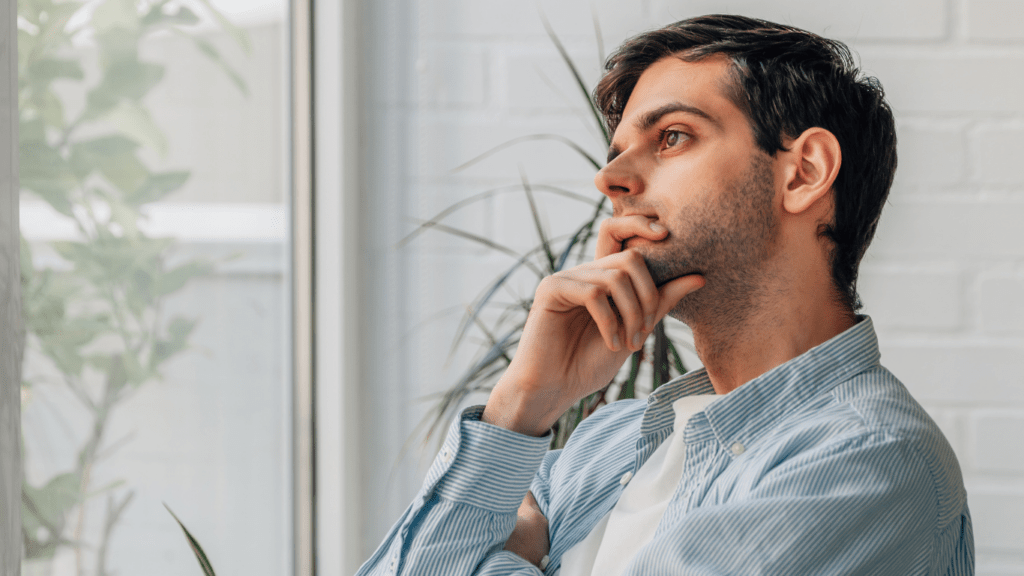 a person sitting in front of a window with their hand on their chin