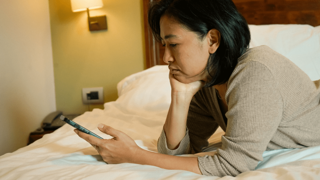 a person laying on a bed looking at a cell phone