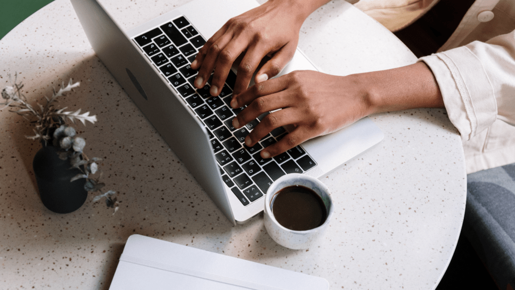 a person typing on a laptop computer with a cup of coffee in front of them